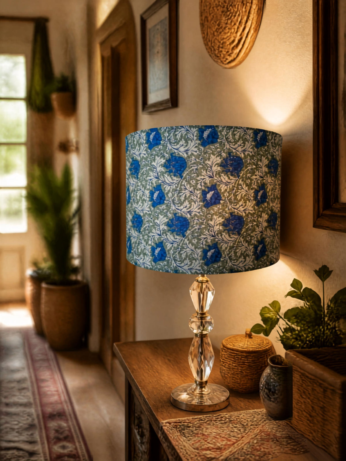 A table lamp with a blue and gray floral patterned drum shade and a faceted crystal base, styled on a wooden console table in a warm, rustic interior.