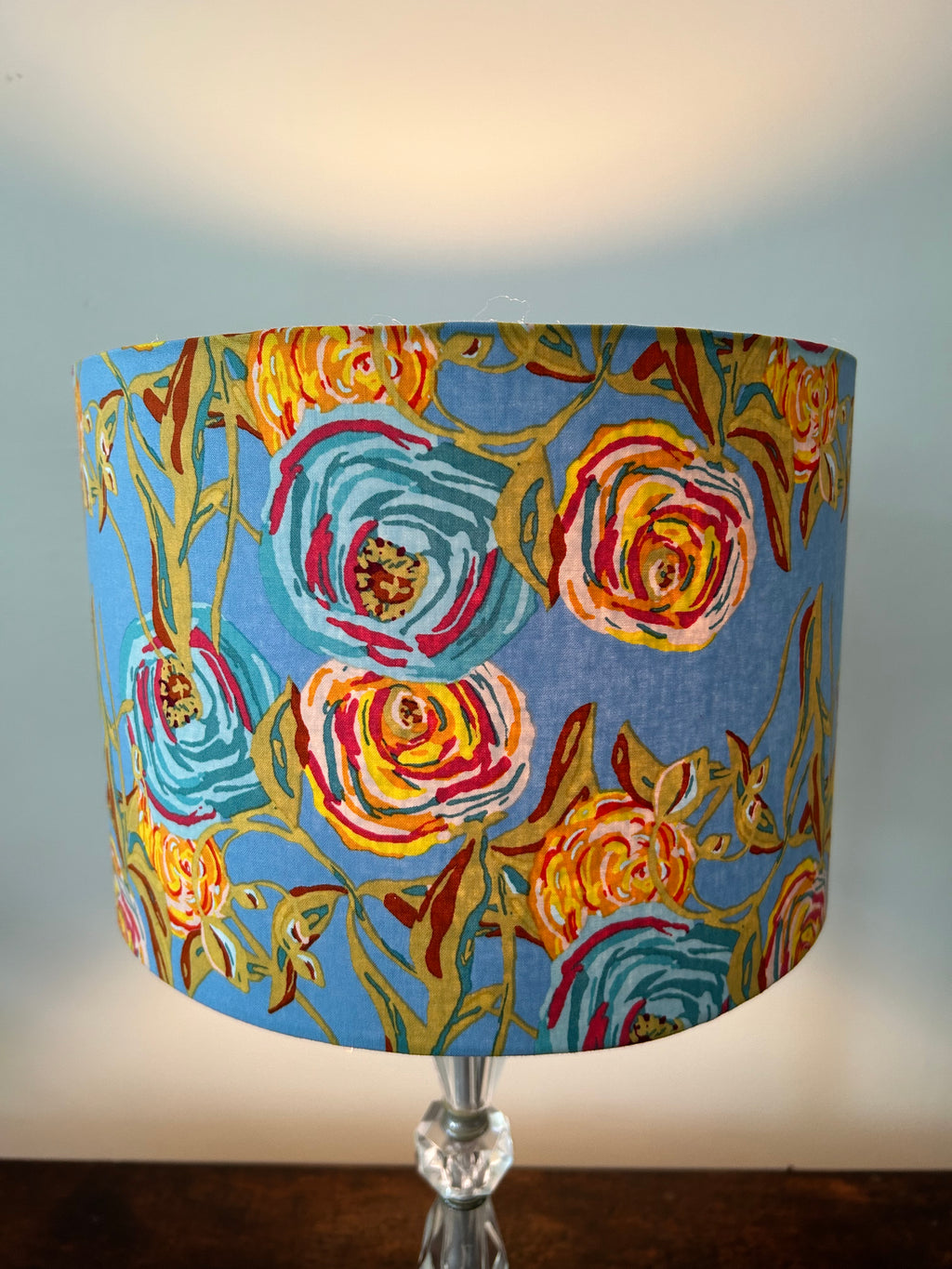 Close-up of a lit Bari J Full Bloom drum lampshade, showing large teal and yellow flowers with pink accents on blue fabric.