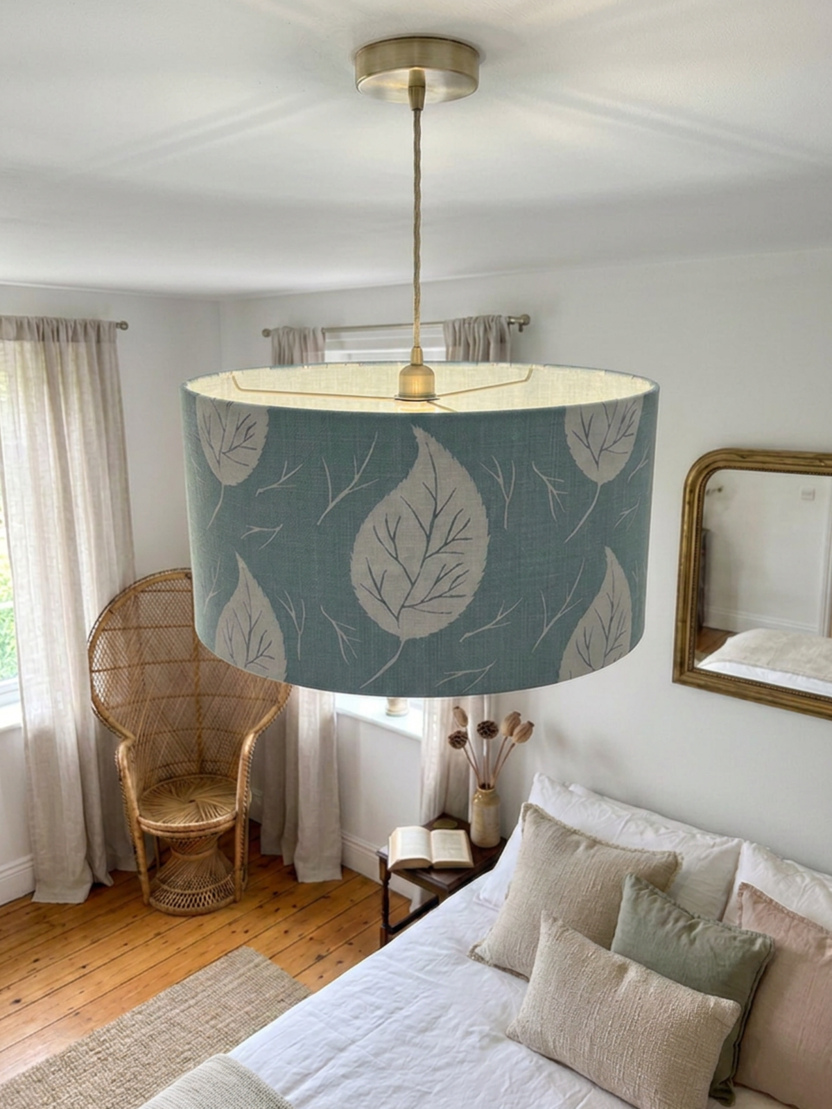 A large drum pendant lamp with a pale blue and white leaf pattern and pale blue lining, hanging in a bright, modern bedroom with a wooden bed, rattan chair, and light wood floors.