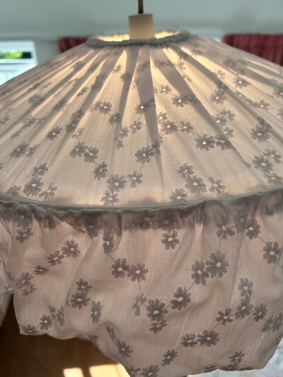 Close up of white broderie anglaise fabric frilly pendant lampshade with light on. The glow is radiating through the fabric softly lighting the room.