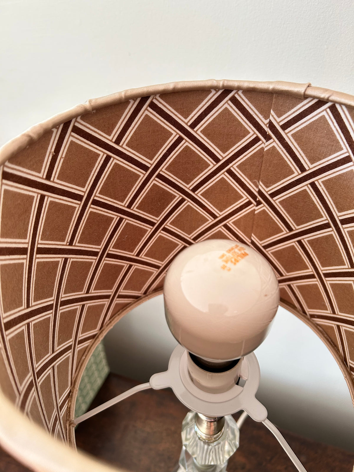 Close-up of a lampshade interior with a brown and beige geometric lattice pattern, showing a white bulb socket and a clear glass finial.
