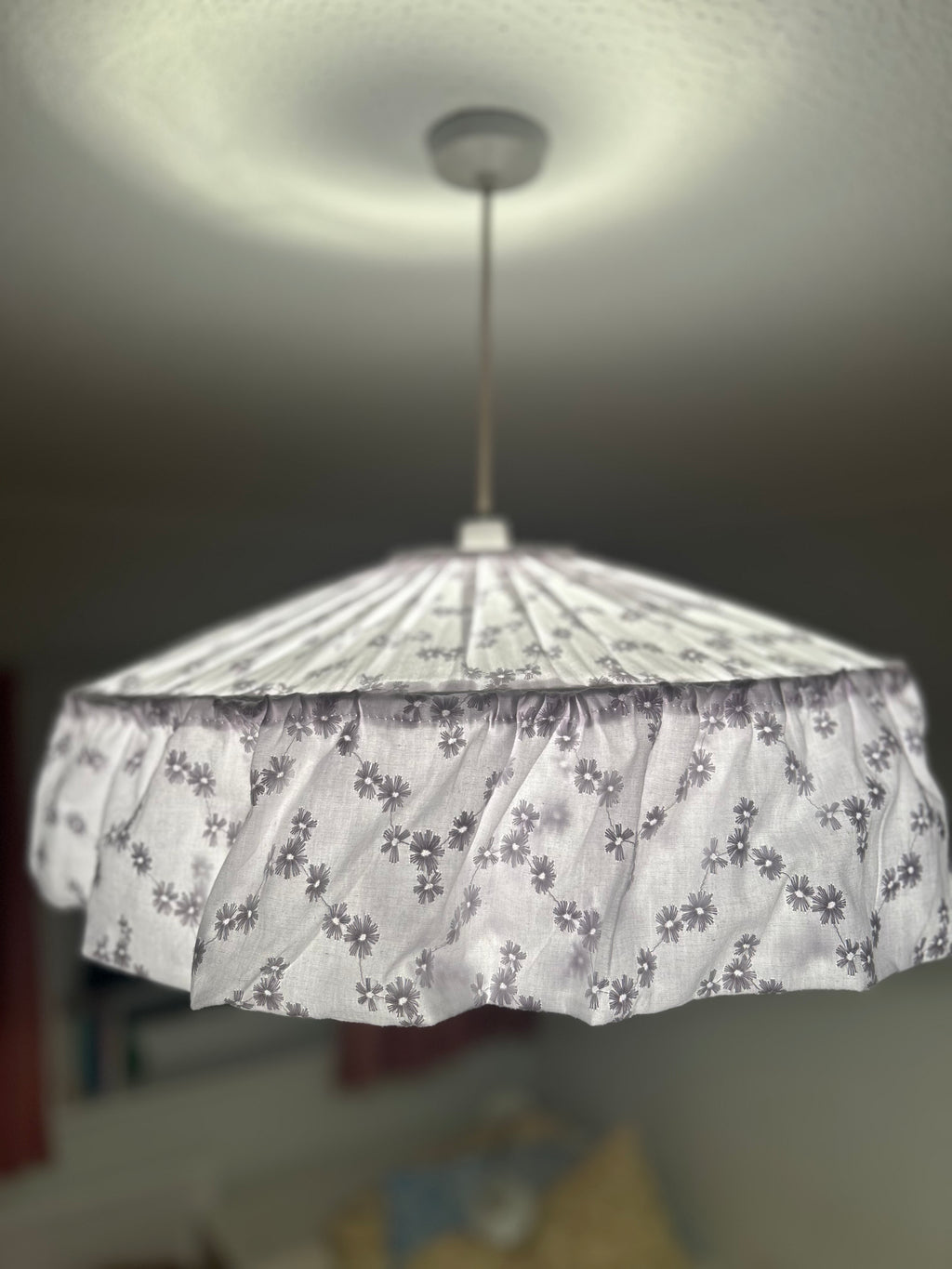 A ruffled fabric chandelier shade with a small floral pattern, hanging from a ceiling in a home interior.