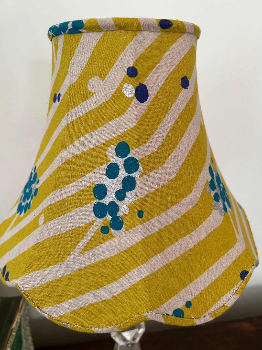 Front close-up of a lime-green empire lampshade, showing cream stripes, teal and navy dots, and its scalloped lower edge.