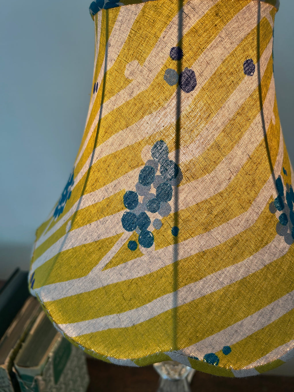 Close-up of a lit empire lampshade, showing the linen weave, lime-green and cream stripes, teal dots and frame ribs.