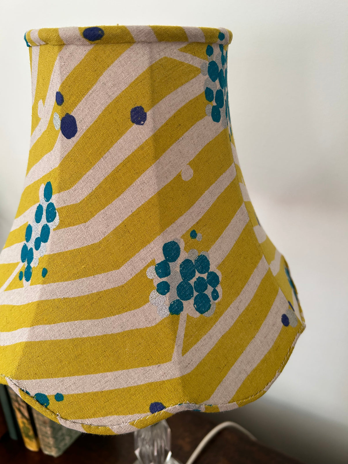 Side close-up of a lime-green linen empire lampshade, with curved cream stripes, teal dot clusters and bound edges.