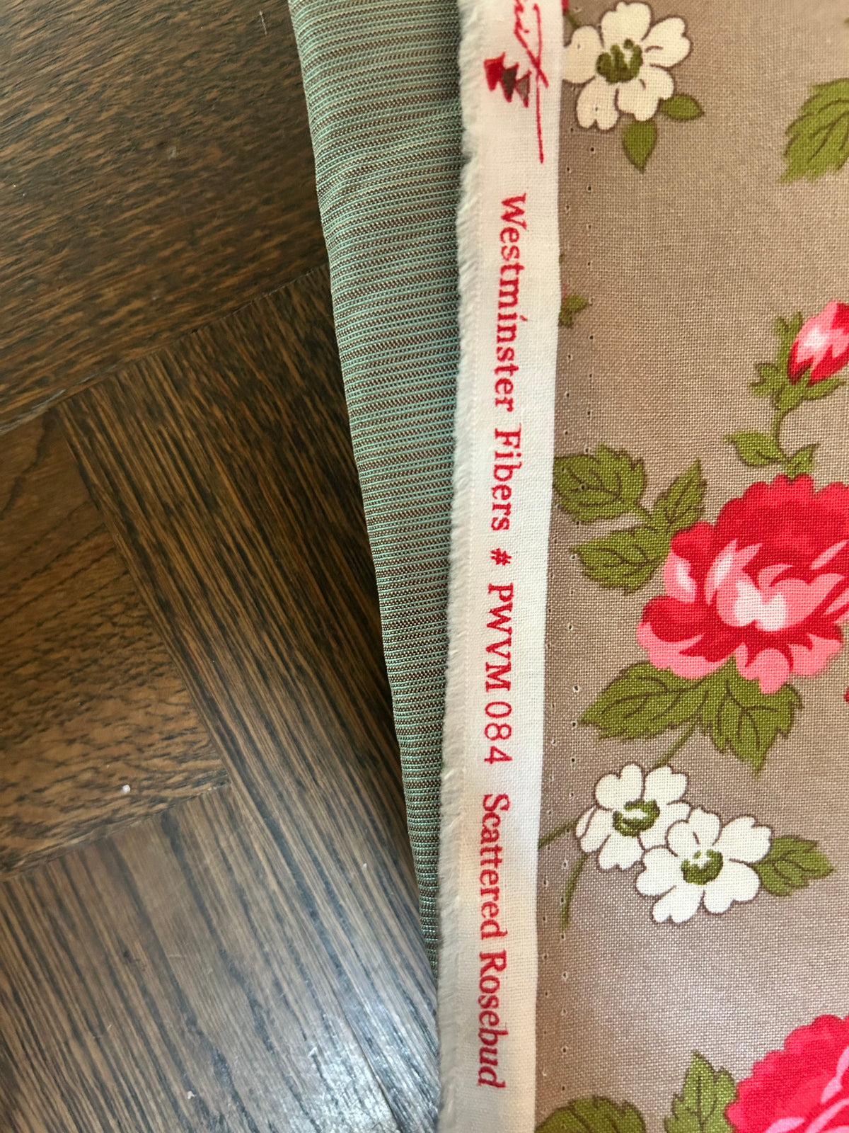 Scattered Rosebud fabric with red roses on a taupe background, beside its selvedge labelled Westminster Fibers.