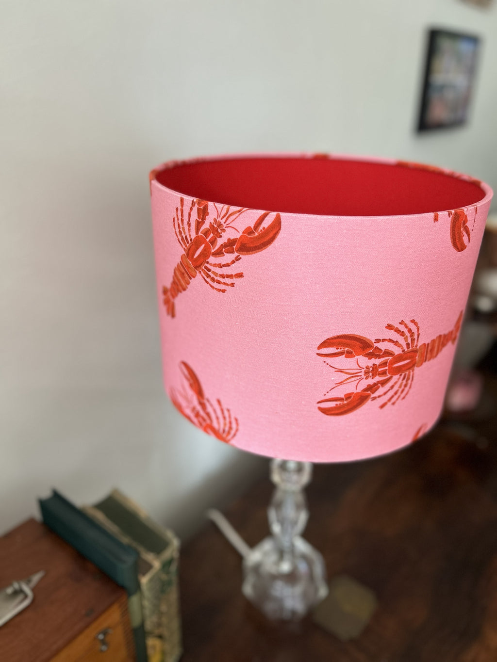 A pink fabric lampshade with a red lobster pattern, shown on a clear glass table lamp in a home setting.