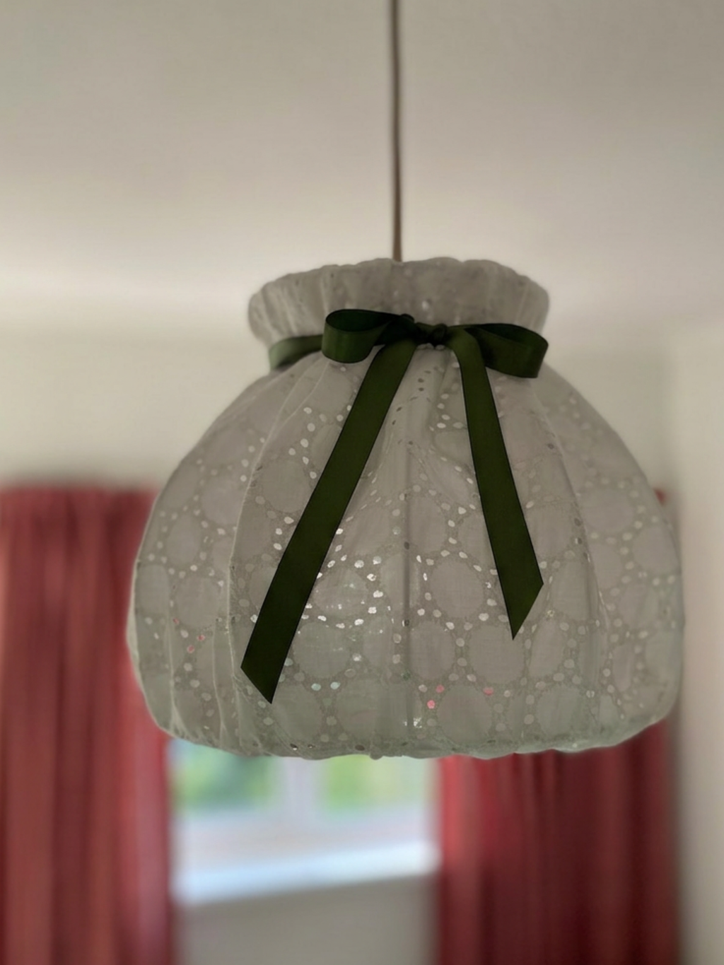 White broderie anglaise pendant lampshade with a gathered top, rounded panels and a sage-green satin bow.