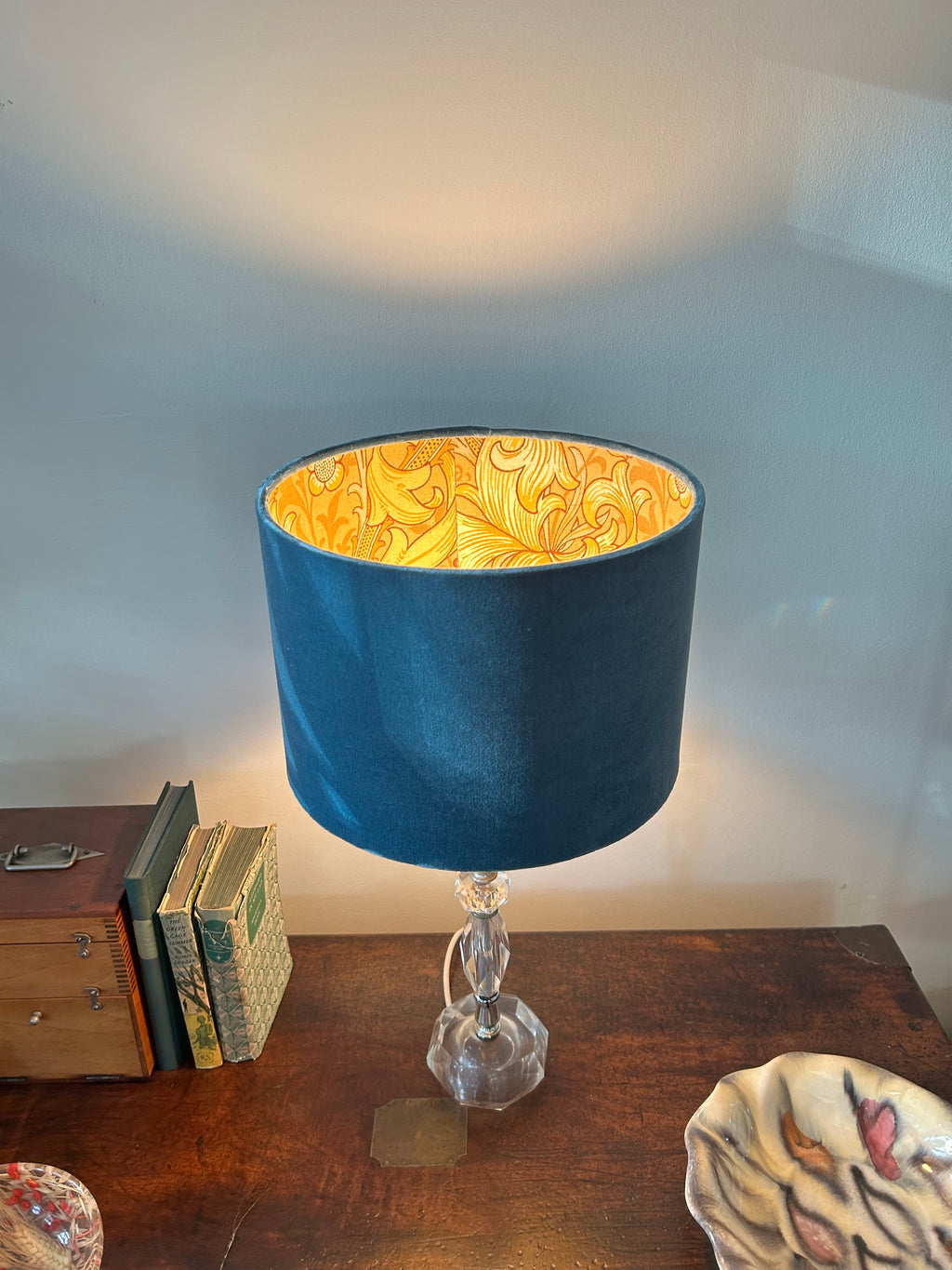 Blue velvet drum lampshade viewed from above with its golden botanical lining illuminated.