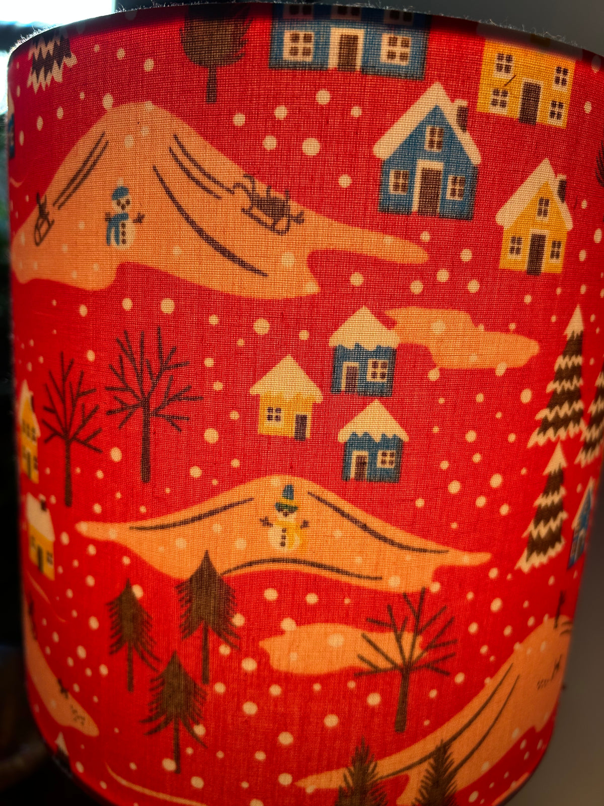 Detail of blue and yellow houses, snowmen and falling snow on the red Christmas lampshade.