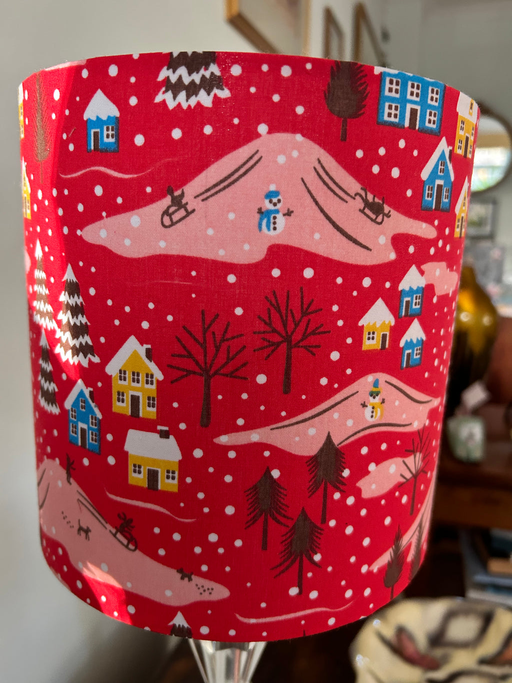 Side view of the Christmas lampshade with sledgers, snowmen and blue houses among pink snowy hills.