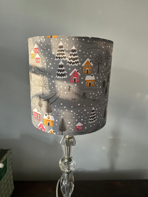 Grey Christmas drum lampshade with raspberry and mustard cottages, snowy fir trees and falling snow.