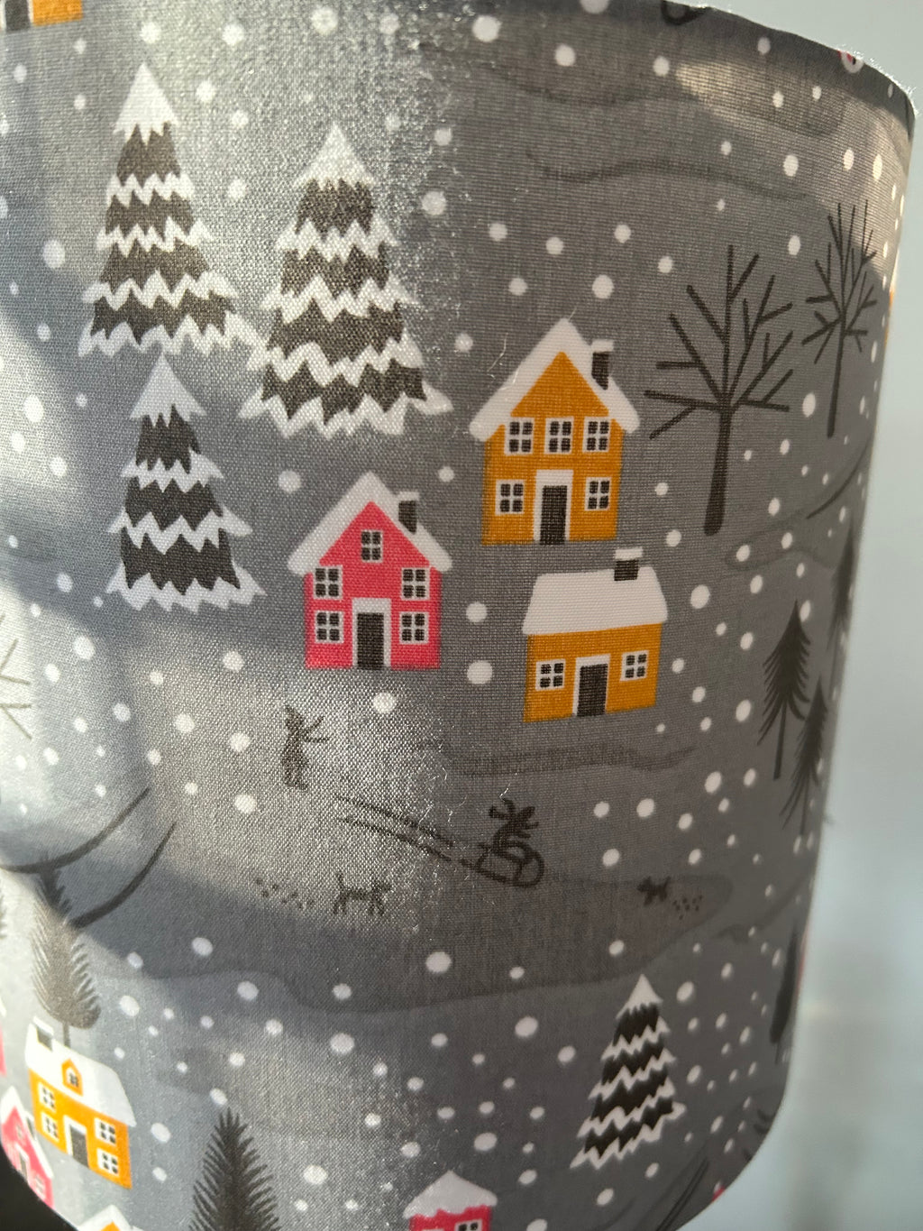 Close-up of raspberry and mustard cottages, snowy fir trees and tiny sledgers on the grey lampshade fabric