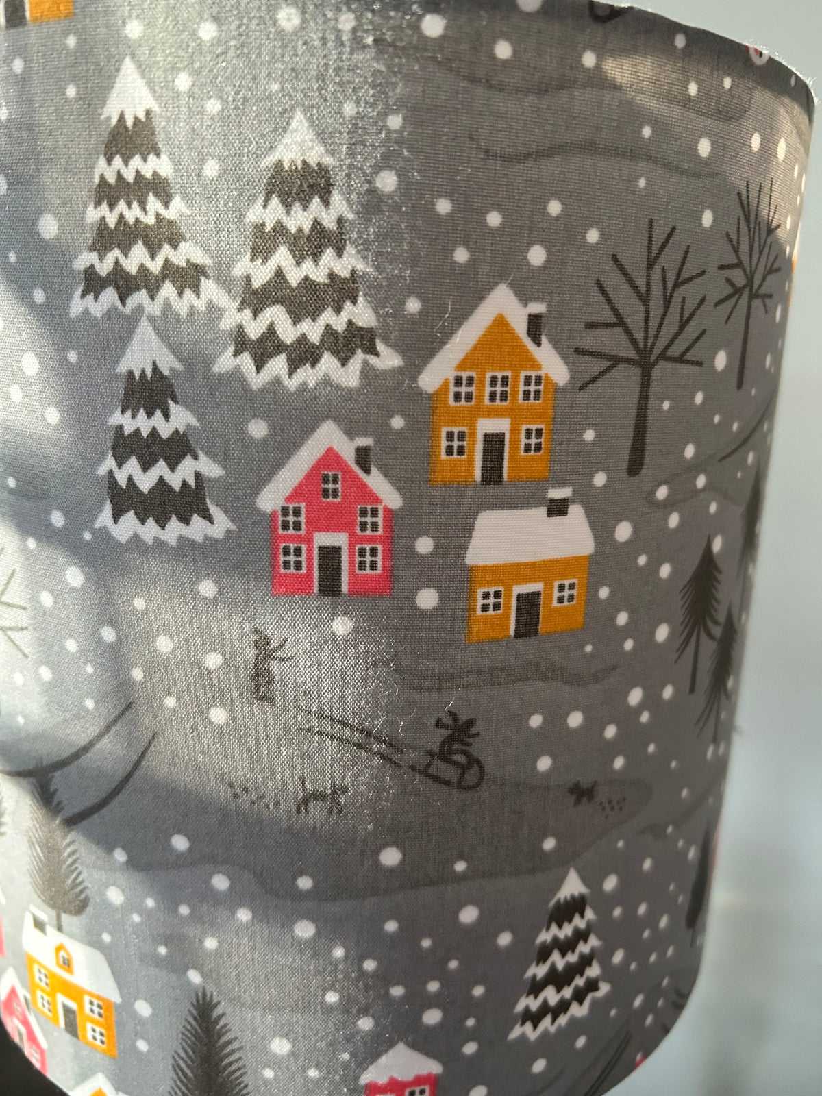 Close-up of raspberry and mustard cottages, snowy fir trees and tiny sledgers on the grey lampshade fabric