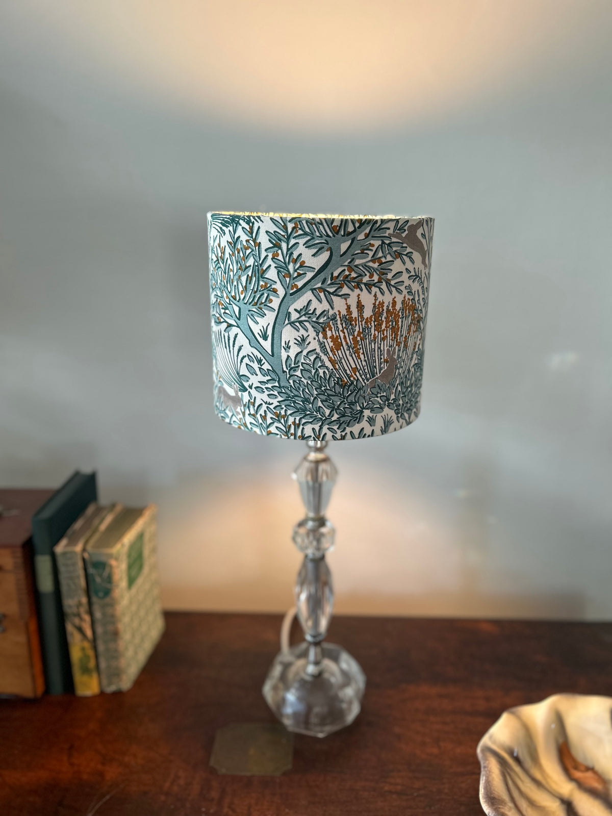 Rabbit-print drum lampshade on a glass lamp base, casting warm light above and below the shade.