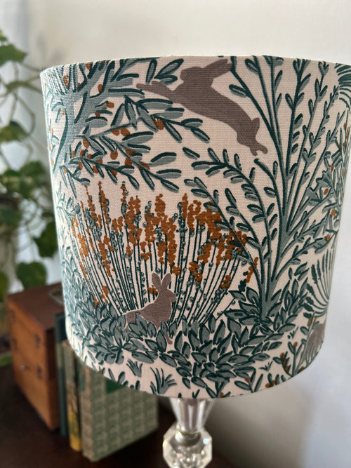 Close-up of grey rabbits, teal foliage and golden seed heads on the white lampshade fabric.