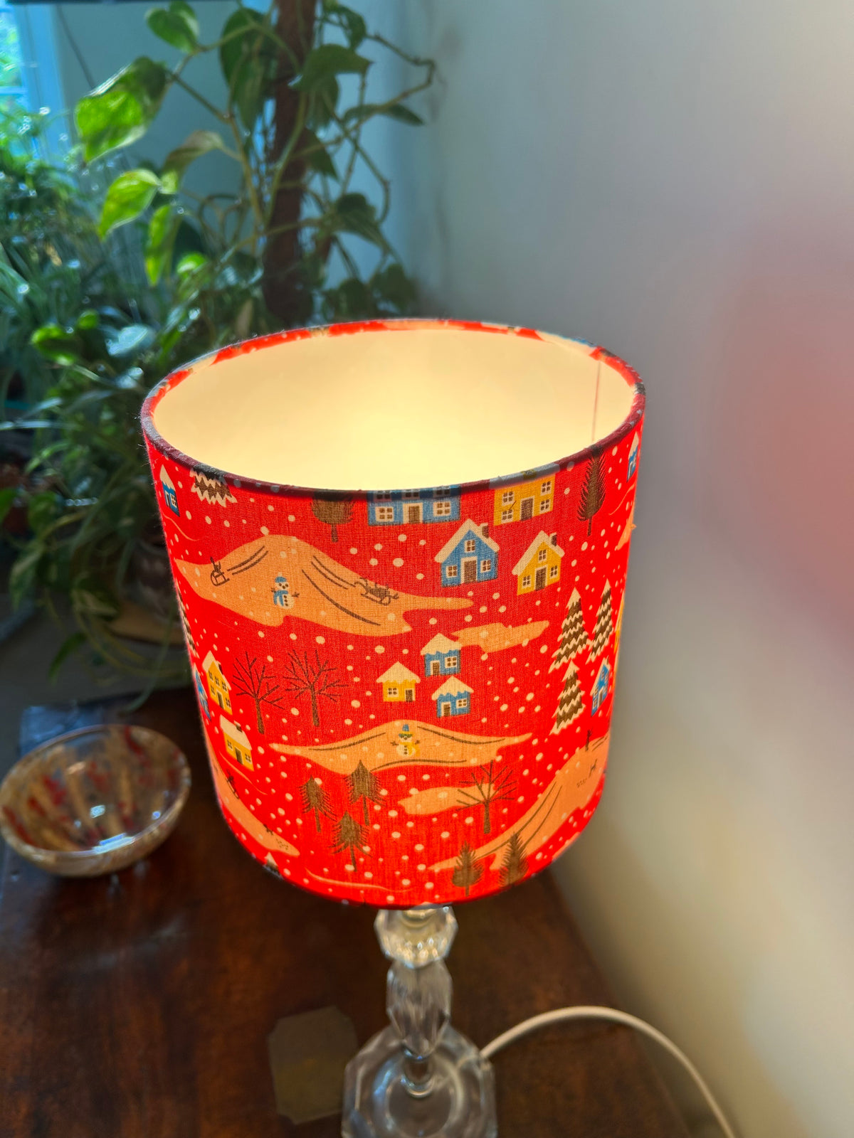 Red snowy village lampshade viewed from above, showing its pale interior glowing when lit.