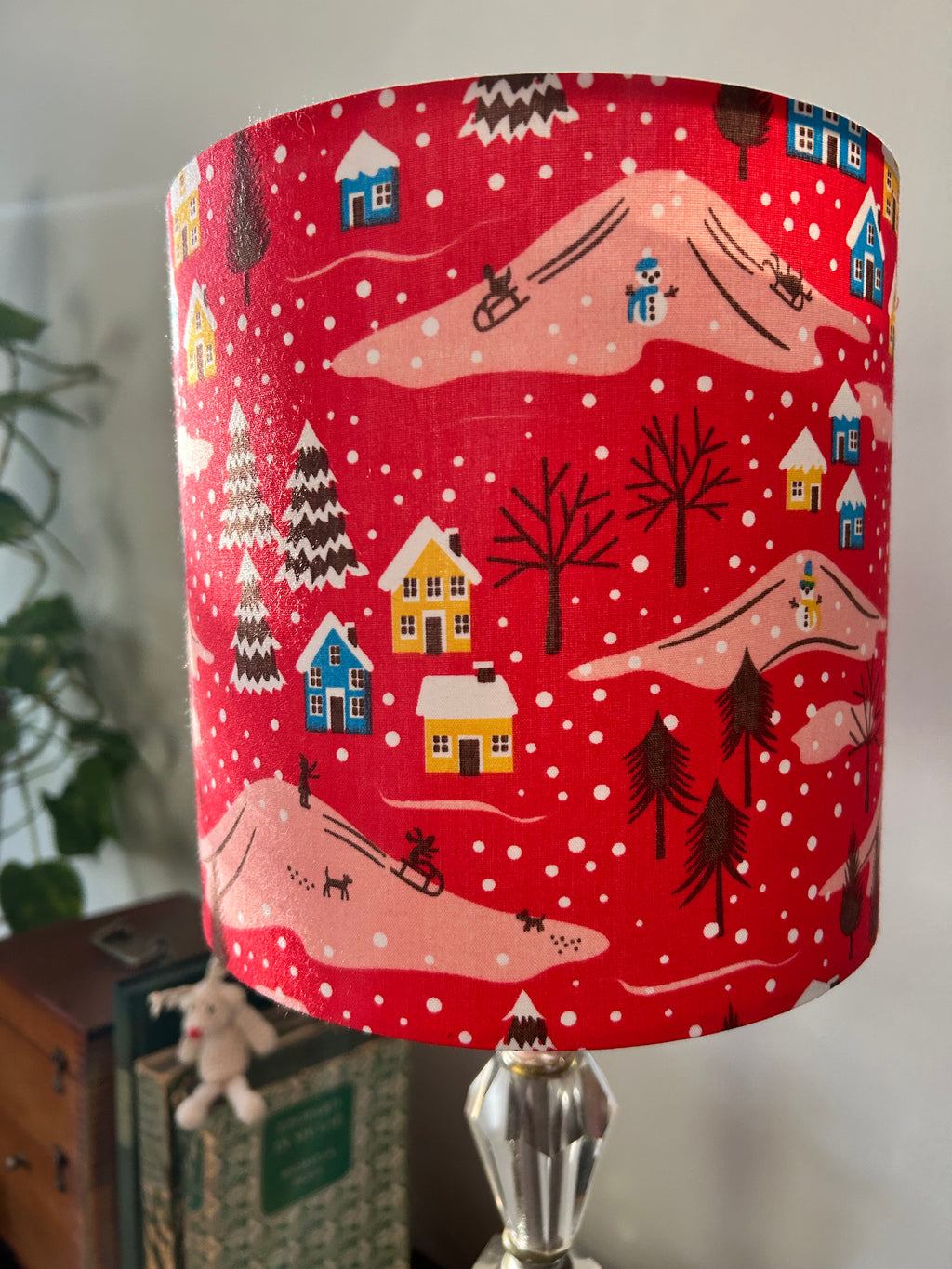 Red lampshade with a winter scene of snowy cottages, bare trees, pink hills and tiny dogs.