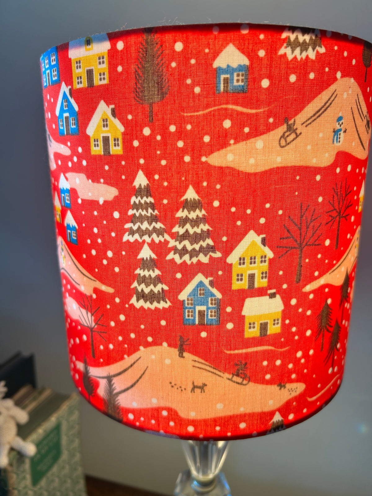 Close-up of the red lampshade fabric showing snow-covered houses, fir trees and sledgers on pink hills.